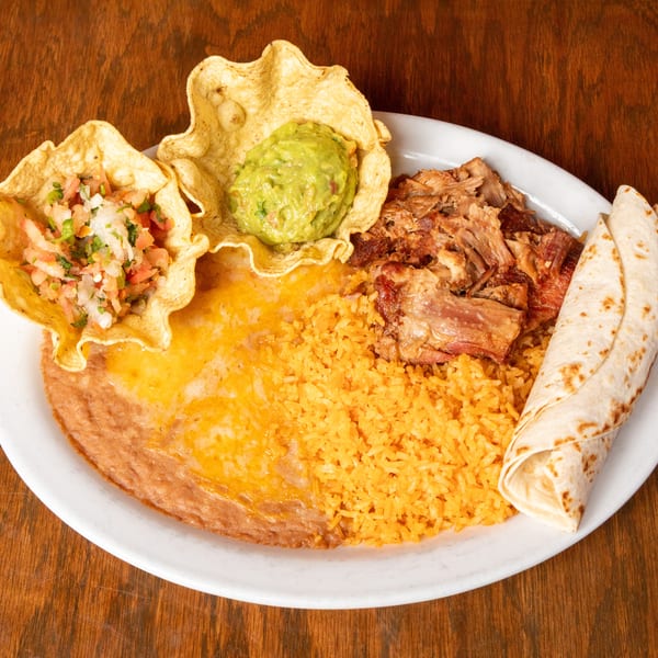 A Mexican dish with carnitas, rice, refried beans, guacamole, pico de gallo, and tortillas.