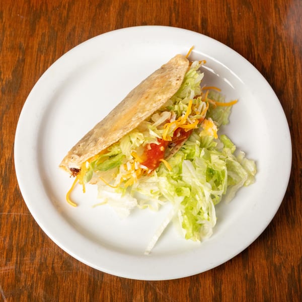 A fried taco with lettuce, cheese, and salsa, served on a white plate.
