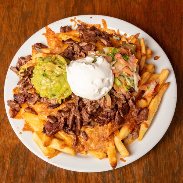 Carne asada fries topped with guacamole, sour cream, and pico de gallo on a white plate.