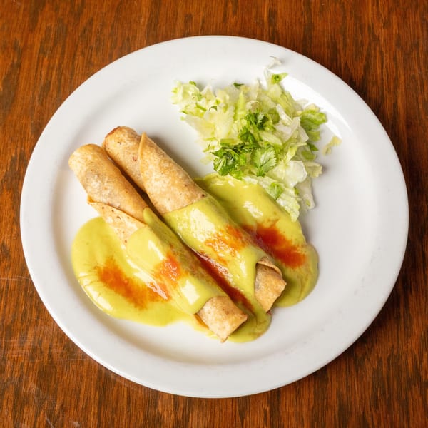 Three taquitos covered in green sauce and red hot sauce, with a side of shredded lettuce.