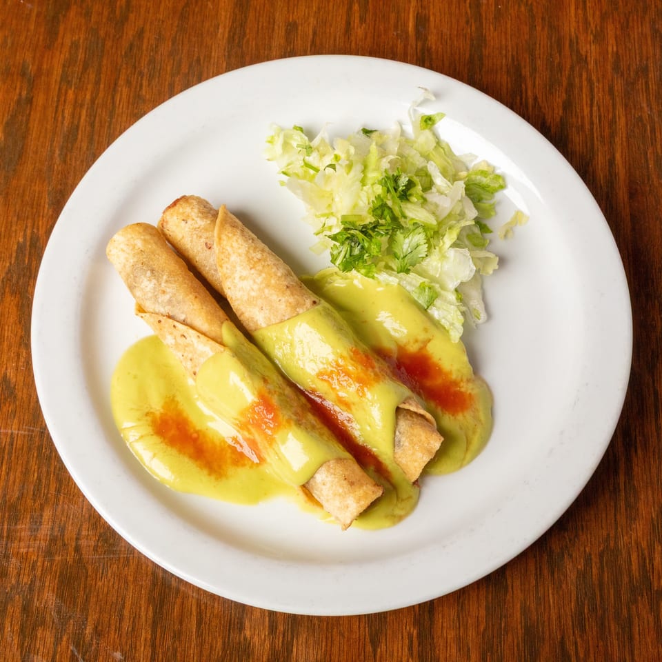 Three taquitos covered in green sauce and red hot sauce, with a side of shredded lettuce.