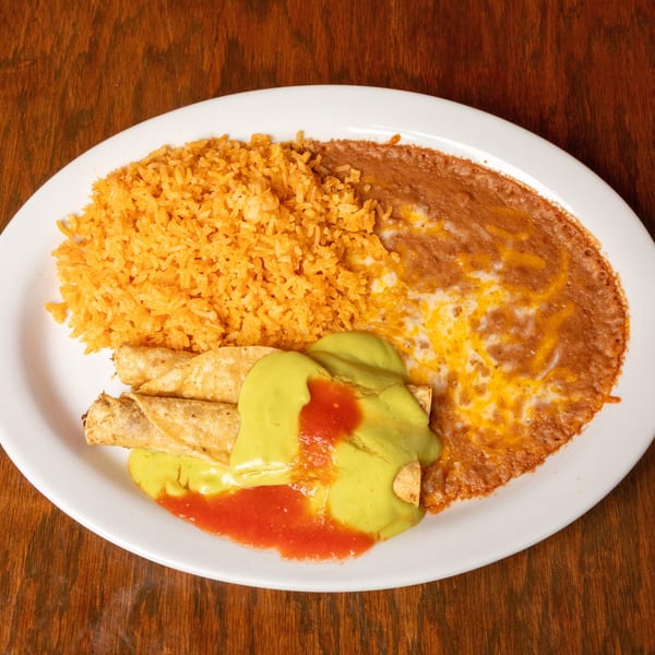 A white oval plate holds golden rice, refried beans with melted cheese, and taquitos with green and red sauce.