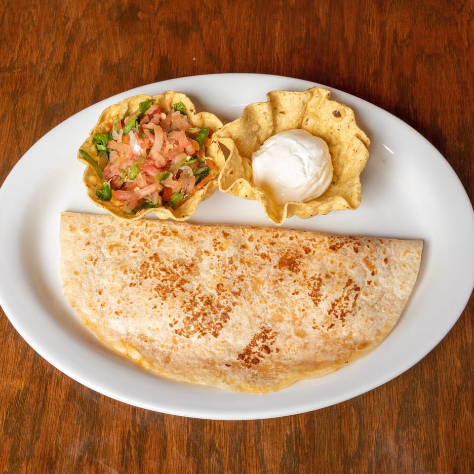 A quesadilla with pico de gallo and sour cream in tortilla bowls on a white plate.