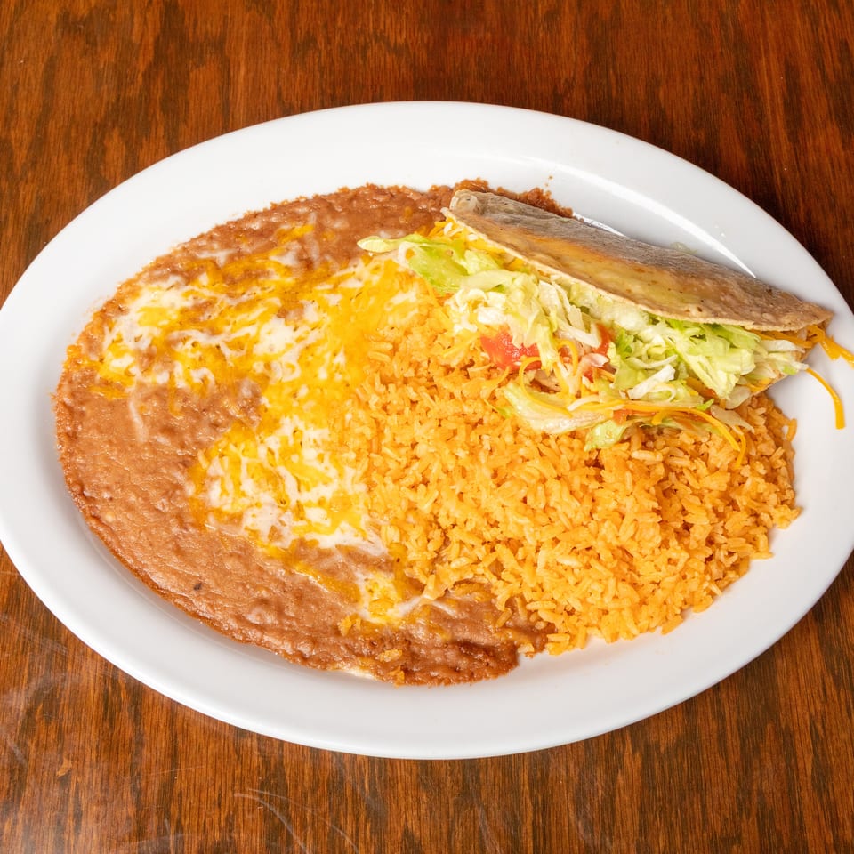 A white plate with a crispy taco, refried beans with melted cheese, and orange Spanish rice.