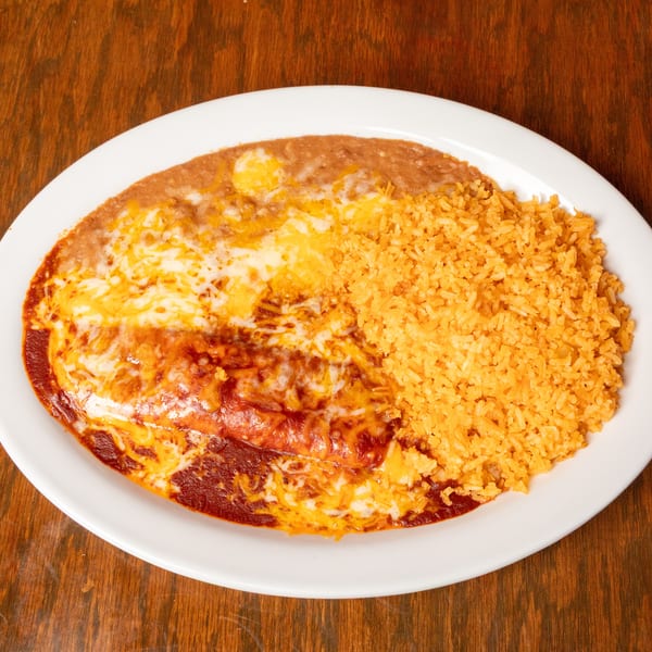 A white oval plate holds cheesy enchiladas, refried beans, and orange Mexican rice on a wooden table.